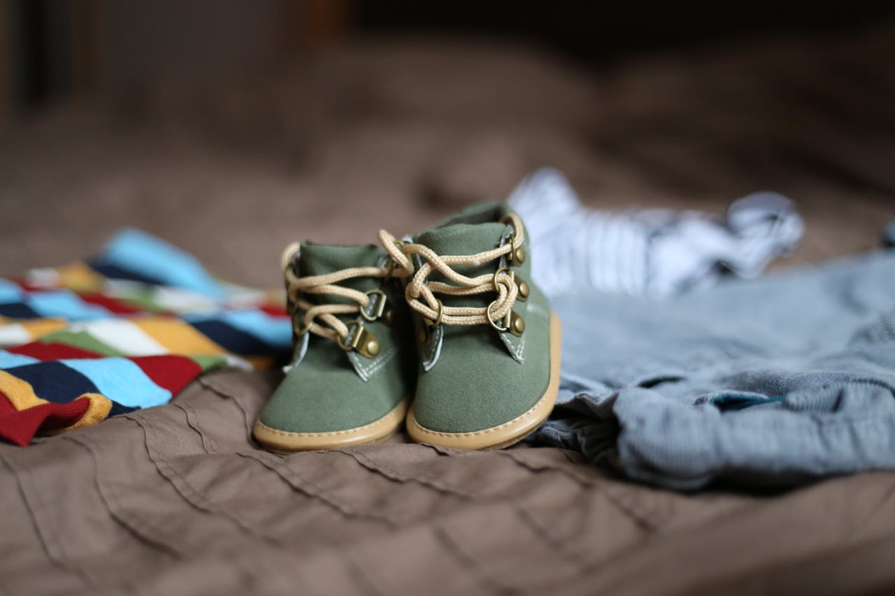 why-choose-us Adorable green baby booties surrounded by colorful clothes, perfect for infant fashion.